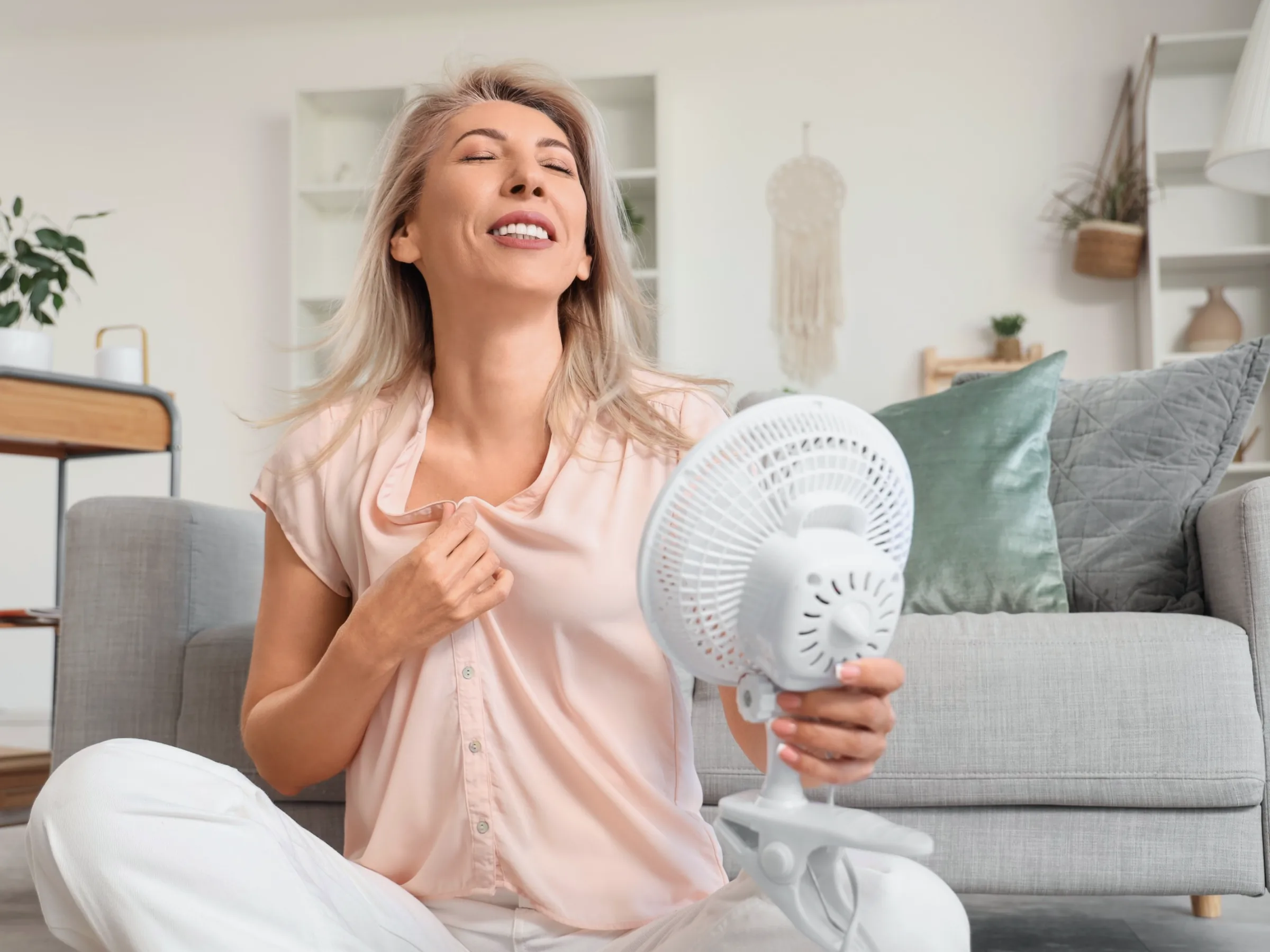 A woman cooling off in front of a small fan at home